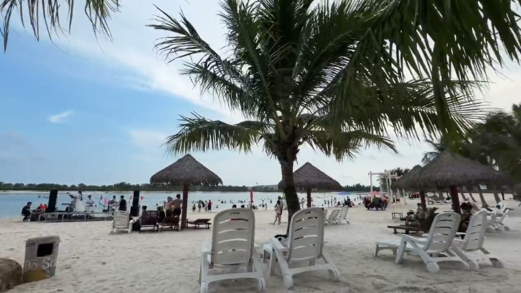 Bãi tắm Đồ Sơn với hàng dừa, ô che lợp lá và ghế nằm trên cát, phía xa khách đang tắm biển