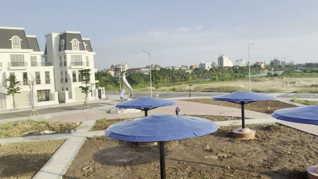 Góc cuối dãy liền kề 24 phân khu River Park với hai mặt thoáng, tường trắng mái xám, cây xanh mới trồng trên vỉa hè và vạch kẻ vàng trên mặt đường nội khu