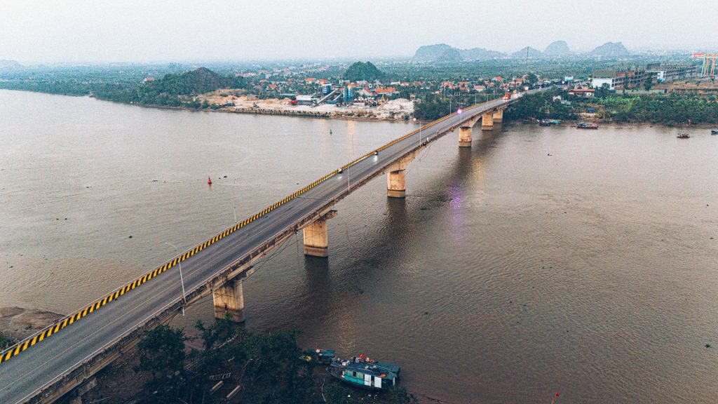 Cầu Đá Bạc hai làn xe bắc qua sông Đá Bạch nhìn từ trên cao, phía xa là dãy núi đá vôi và khu dân cư ven sông