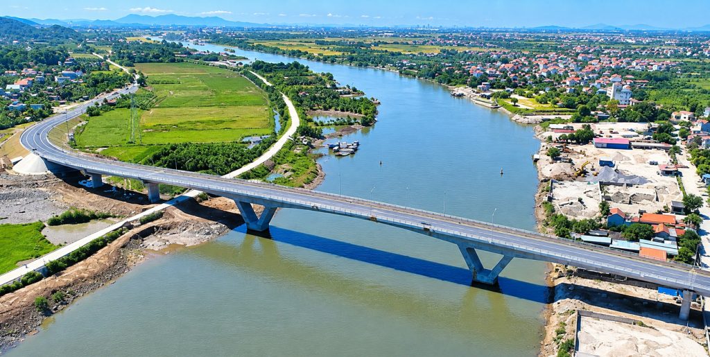 Cầu Dinh uốn cong qua sông Kinh Thầy nhìn từ trên cao, một bên là cánh đồng xanh, bên kia là khu dân cư mái đỏ ven sông