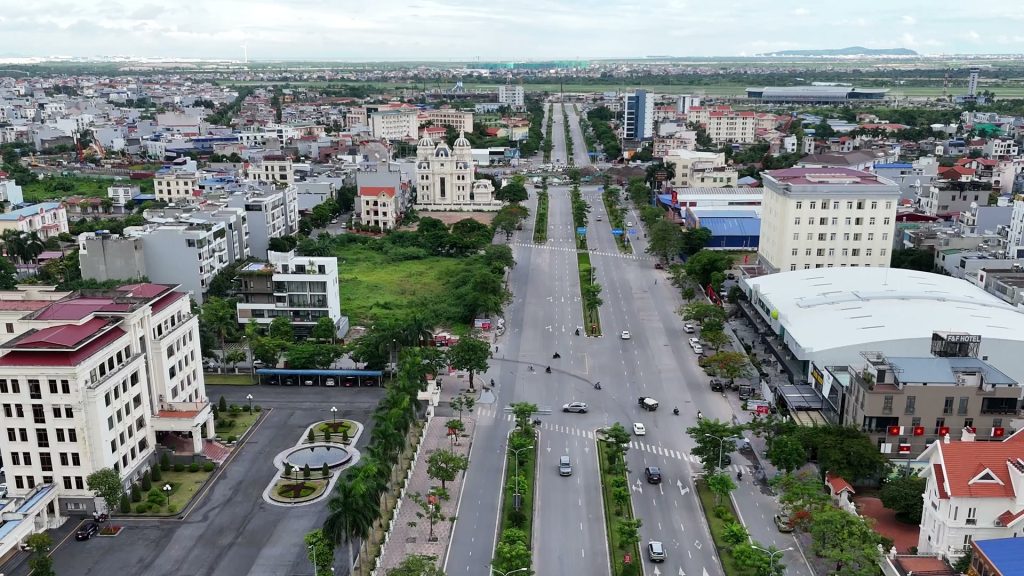 Đại lộ rộng với các dải phân cách trồng cây chạy thẳng về phía xa, hai bên là toà văn phòng, nhà phố và một toà nhà mái trắng lớn, nhìn từ trên cao