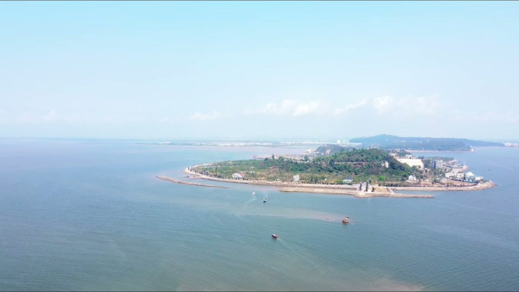 Đảo Hòn Dấu ở Đồ Sơn nhìn từ trên cao, hòn đảo phủ cây xanh nhô ra giữa biển với dải bờ đá bao quanh