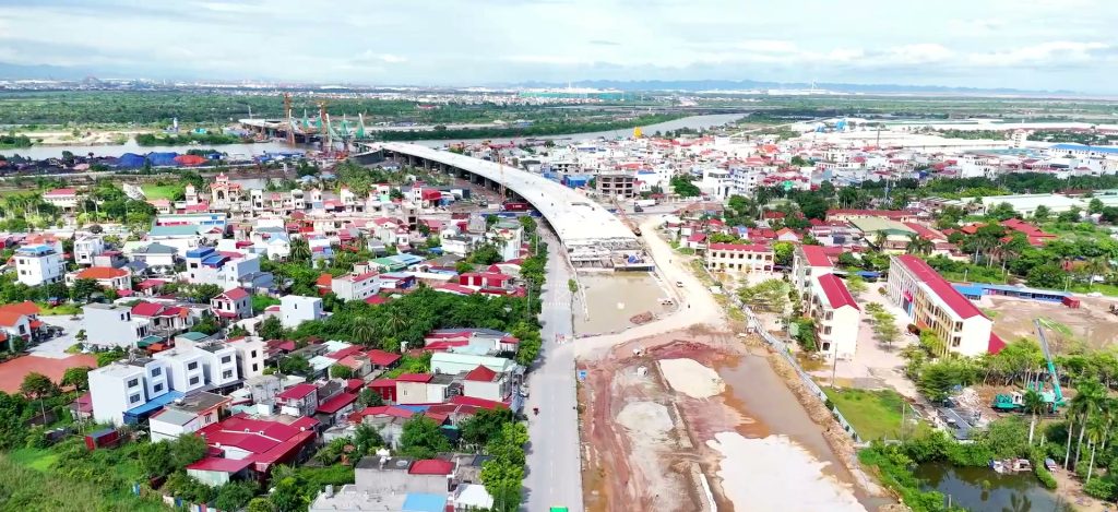 Một đoạn tuyến đường mới đang thi công nhìn từ trên cao, chạy song song con đường cũ, hai bên là khu dân cư và các dãy nhà xưởng