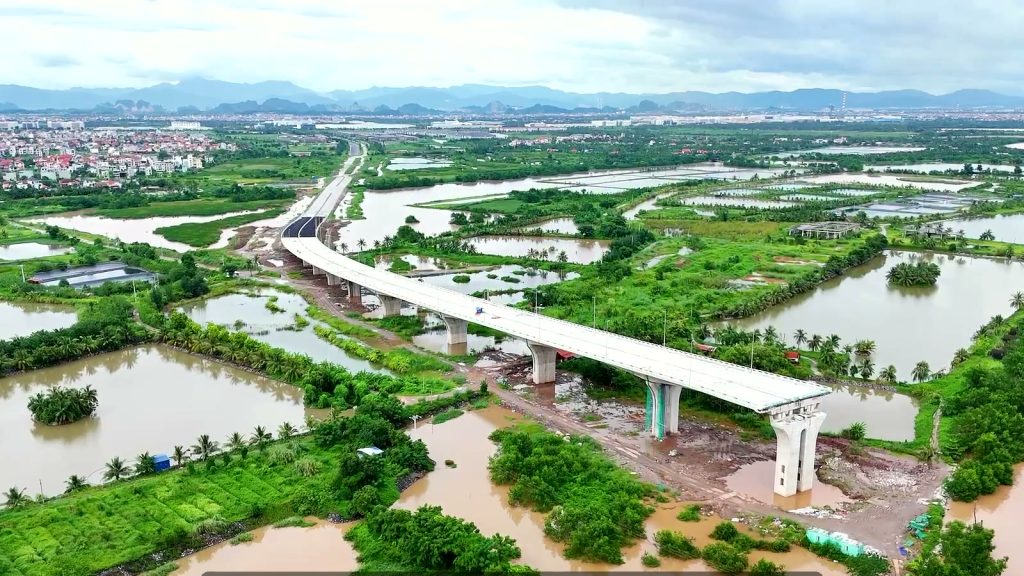 Đường dẫn trên cao phía bờ bắc sông Cấm vươn qua vùng đầm nước và cây xanh, nối vào trục đường thẳng dẫn về khu đô thị phía sau