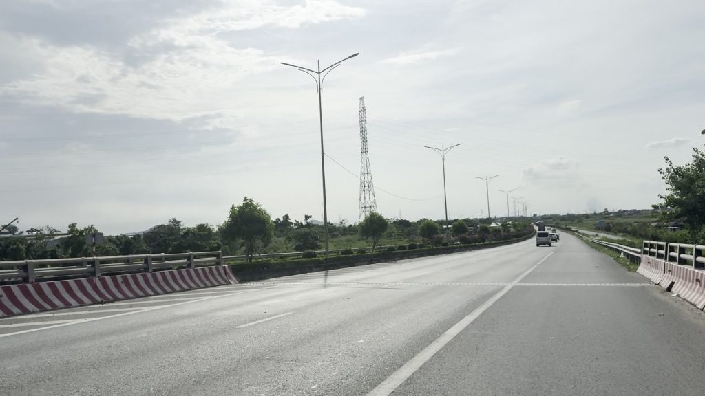 Mặt đường mới rộng nhiều làn chạy giữa đồng ruộng với dải hộ lan sơn đỏ trắng và hàng cột đèn cao áp mới dựng