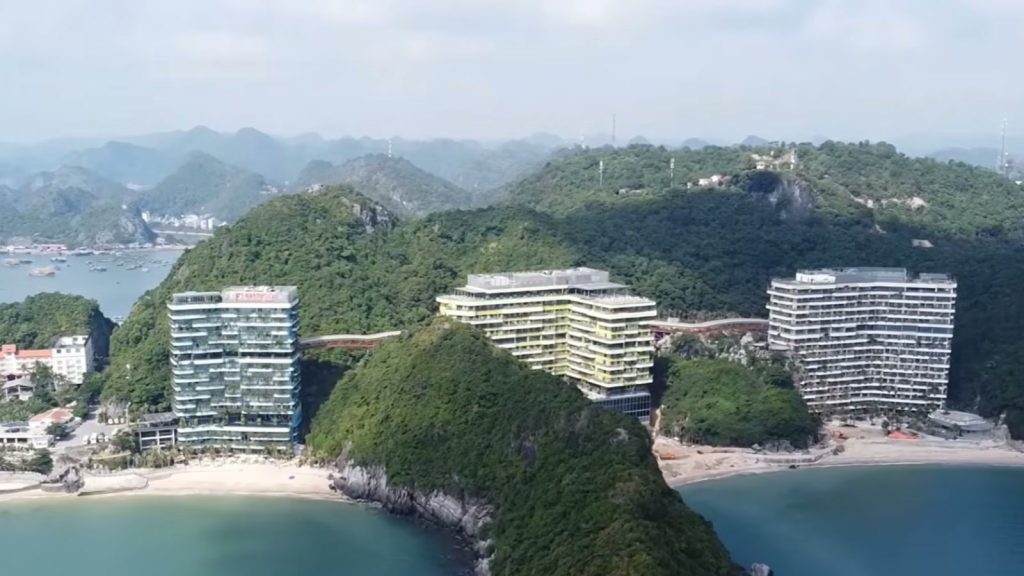 Ba tòa tháp khu nghỉ dưỡng Flamingo Cát Bà, khách sạn 5 sao Hải Phòng nằm giữa hai bãi biển Cát Cò, phía sau là núi đá vôi phủ rừng và vịnh có thuyền neo
