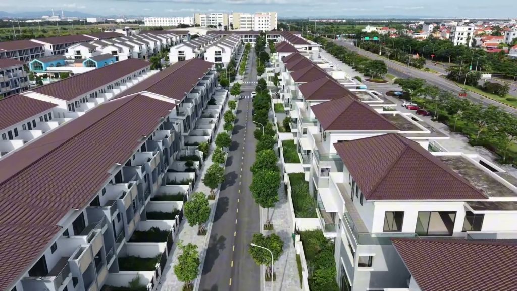 Dãy nhà liền kề mái nâu hai bên một con đường có hàng cây xanh trong khu nhà ở cạnh khu công nghiệp, nhìn từ trên cao