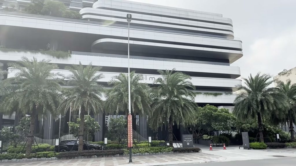 Khối đế Pullman Hải Phòng với các tầng bo cong màu trắng xếp chồng, cây xanh rủ trên sân thượng, hàng cây chà là trồng dọc vỉa hè phía trước