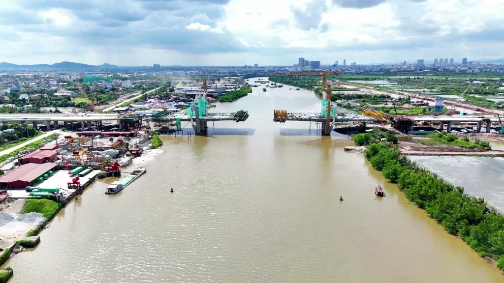 Sông Lạch Tray nhìn từ trên cao, sà lan neo dọc bờ trái, phía xa là hai nửa cầu Hải Thành đang thi công vươn ra giữa sông