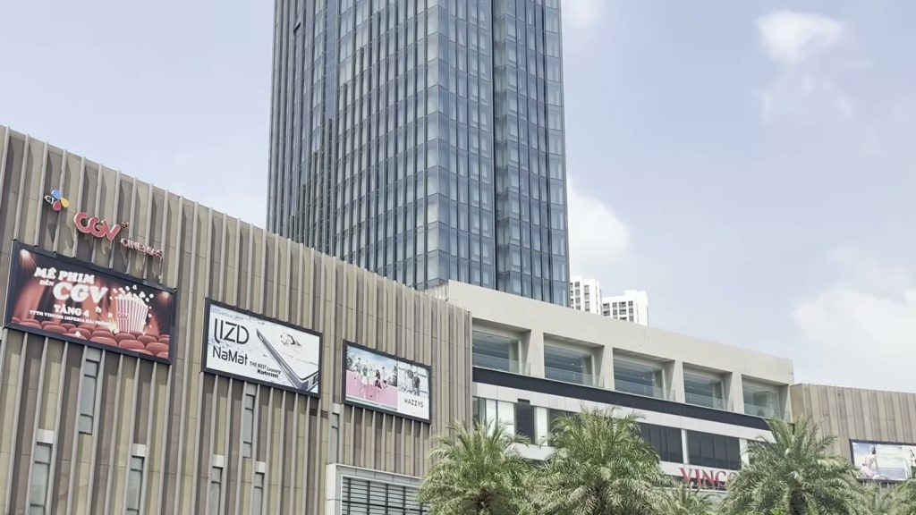 Tòa tháp kính xanh thẫm của khách sạn Sheraton Hải Phòng vươn cao trên nền trời nhiều mây, phía dưới là tán cây xanh