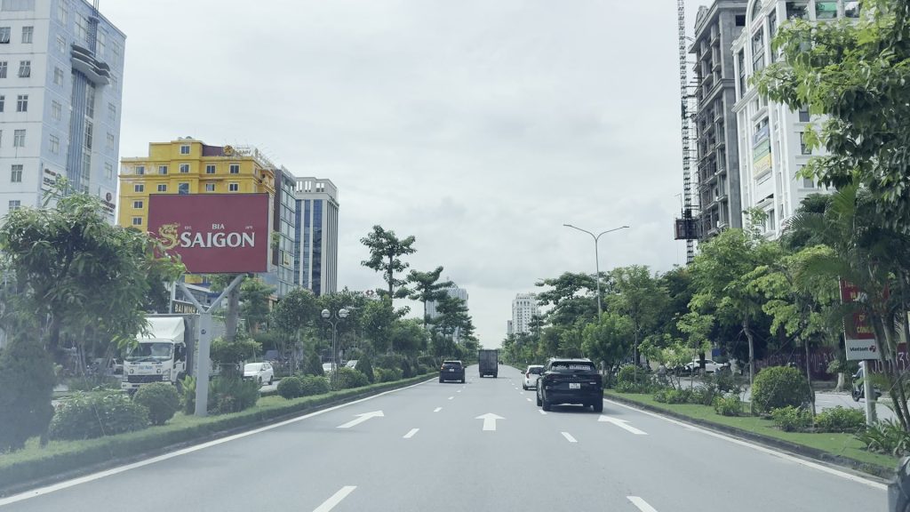 Trục đường lớn nội thành Hải Phòng nhiều làn xe với dải phân cách trồng cây, ô tô và xe tải chạy giữa hai hàng nhà cao tầng
