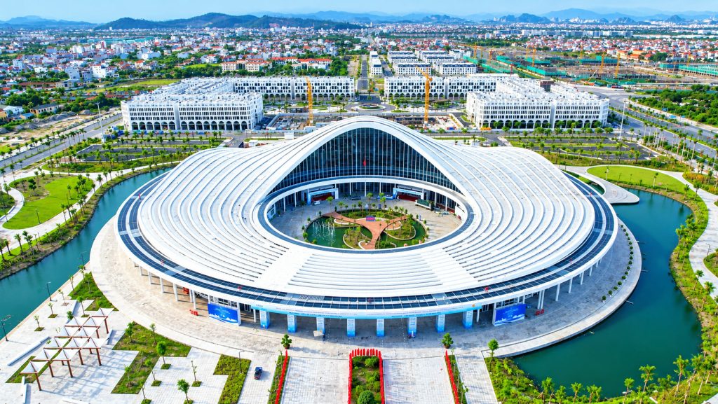 Trung tâm Hội nghị Biểu diễn Hải Phòng nhìn từ trên cao, mái trắng hình giọt nước nằm giữa hồ, phía sau là khu trung tâm hành chính và khu đô thị mới