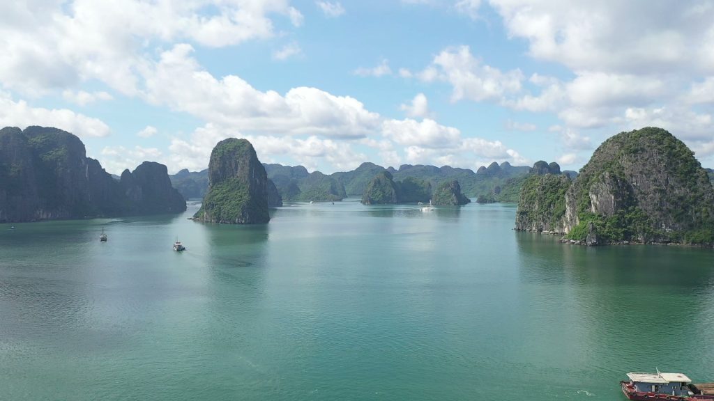 Vịnh Hạ Long với những khối núi đá vôi nhô lên mặt nước xanh, một chiếc thuyền nhỏ chạy giữa vịnh