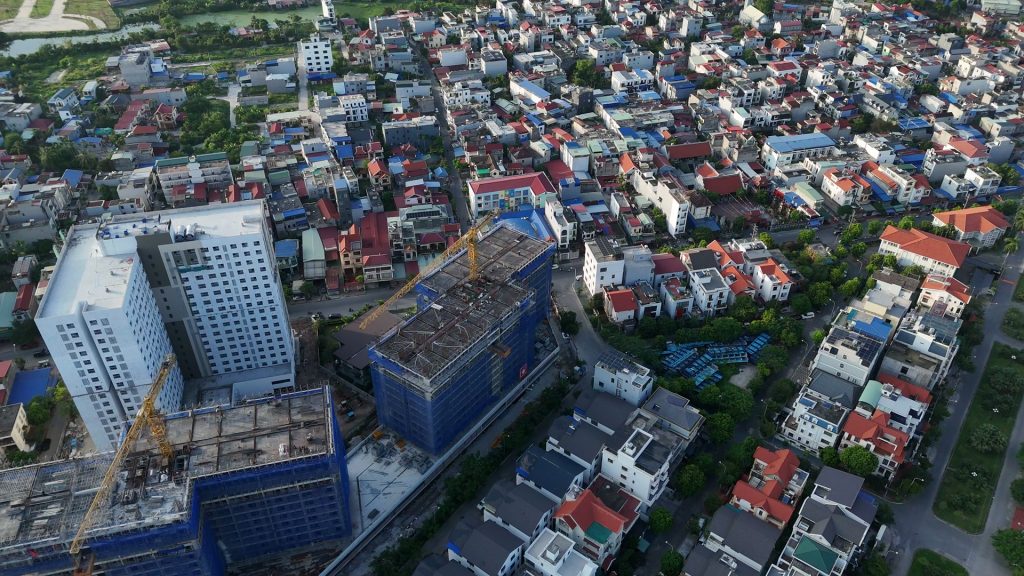 Ba khối nhà của AnZen Residences nhìn từ trên cao giữa khu dân cư thấp tầng mái đỏ, một khối đã hoàn thiện và hai khối còn giàn giáo