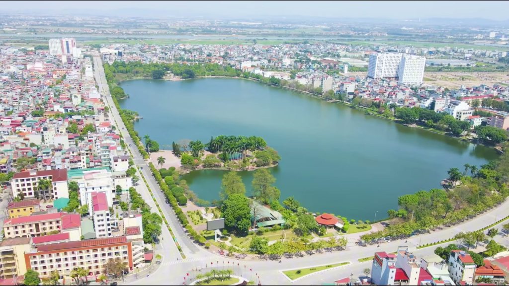 Hồ nước lớn nằm giữa khu phố ở Thuỷ Nguyên nhìn từ trên cao, một đảo cây xanh ở giữa hồ, hai bên là nhà ống và trục đường chạy dọc bờ