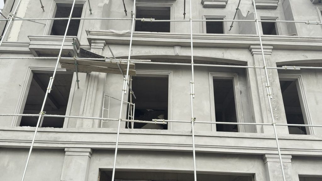 Mặt ngoài căn liền kề LK06-19 cao 5 tầng, tường còn màu vữa xám chưa sơn, giàn giáo dựng kín mặt tiền