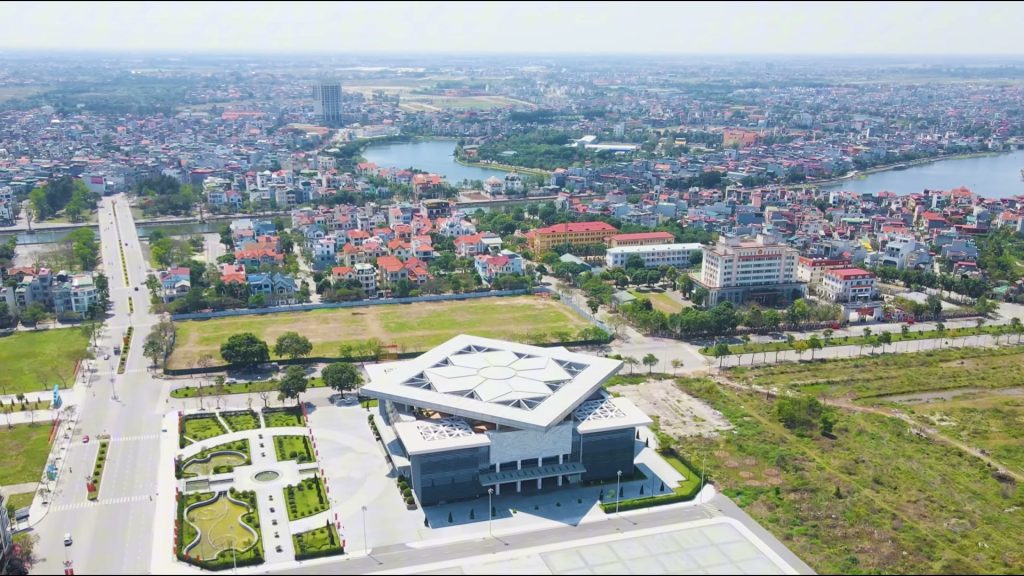 Trung tâm hành chính vùng Thuỷ Nguyên nhìn từ trên cao, toà nhà mái hình thoi màu trắng đứng giữa quảng trường và khu dân cư mái đỏ